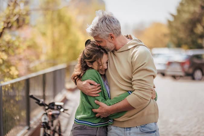 Teenage daughter hugging her father outside in town when spending time together