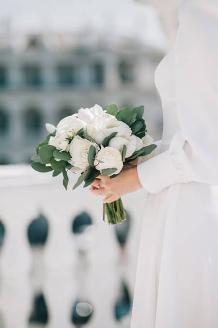 The bride in a white dress holds a delicate wedding bouquet in her hands