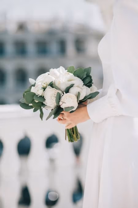 The bride in a white dress holds a delicate wedding bouquet in her hands